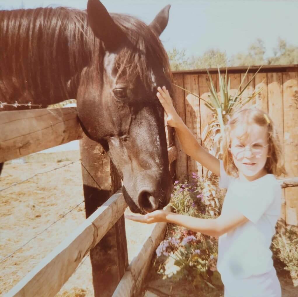 Sandra Daulon enfant caressant la liste d'un grand cheval noir camarguais