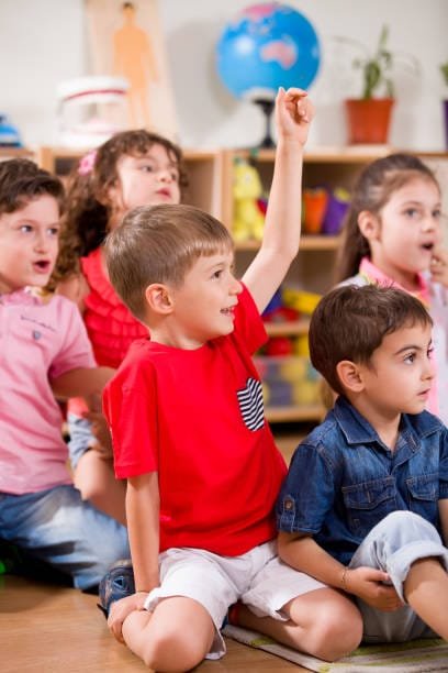 garçon levant le doigt assis au milieu d'un groupe dans une classe